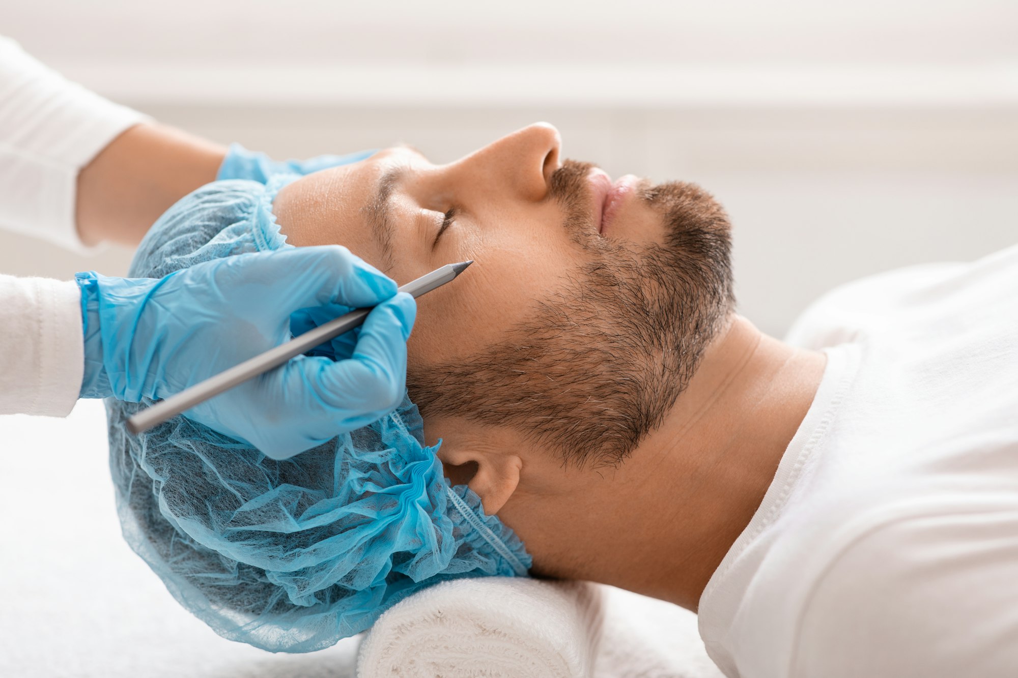 Handsome man getting pencil marks under eyes before surgery