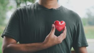 Homme qui tient un Cœur en plastique devant son vrai cœur